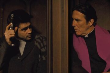 In Bruges 2008 Movie Scene Colin Farrell as Ray holding a gun in a confessional booth next to Ciarán Hinds as Priest