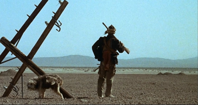 A Boy and His Dog 1975 Movie Scene Don Johnson as Vic holding a rifle and looking into the distance as his dog Blood pees on broken telephone pole