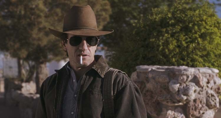 The Rambler 2013 Movie Scene Dermot Mulroney as The Rambler, a drifter who just got out of prison, smoking a cigarette and wearing a cowboy hat and sunglasses