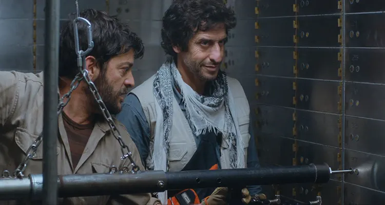 Heist of the Century 2020 Movie Scene Diego Peretti as Fernando Araujo smiling as Pablo Rago as Marciano is using his special machine to break into security deposit boxes