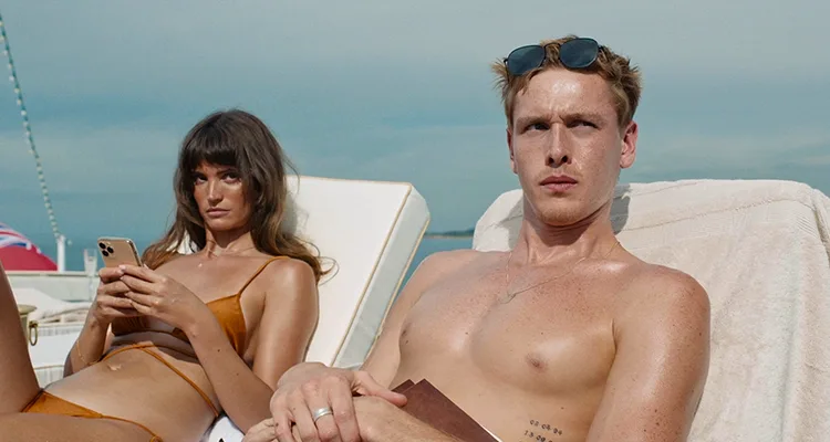 Triangle of Sadness 2022 Movie Scene Harris Dickinson as Carl and Charlbi Dean as Yaya sunbathing on top of a luxury yacht