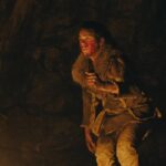 Out of Darkness 2022 Movie Scene Safia Oakley-Green as Beyah all bloody, holding a knife and hiding in a cave