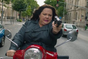 Spy 2015 Movie Scene Melissa McCarthy as Susan Cooper holding a gun while driving a scooter