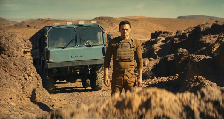 The Wages of Fear 2024 Movie Scene Alban Lenoir as Alex standing in front of a big rock with the truck carrying nitroglycerine in the background
