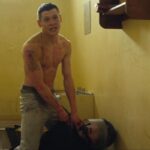 Starred Up 2013 Movie Scene Jack O'Connell as Eric Love in his prison cell holding a guard hostage, oiled up and ready to fight