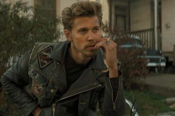 The Bikeriders 2023 Movie Austin Butler as Benny smoking a cigarette and wearing a leather jacket while sitting on his motorcycle