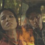 Don't Move 2024 Movie Scene Kelsey Asbille as Iris paralyzed in a car watching a house burning while serial killer Finn Wittrock as Richard looks at her