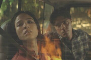 Don't Move 2024 Movie Scene Kelsey Asbille as Iris paralyzed in a car watching a house burning while serial killer Finn Wittrock as Richard looks at her