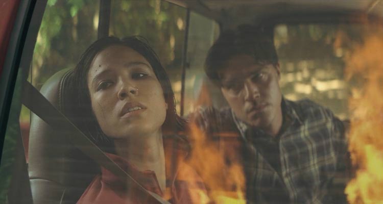 Don't Move 2024 Movie Scene Kelsey Asbille as Iris paralyzed in a car watching a house burning while serial killer Finn Wittrock as Richard looks at her