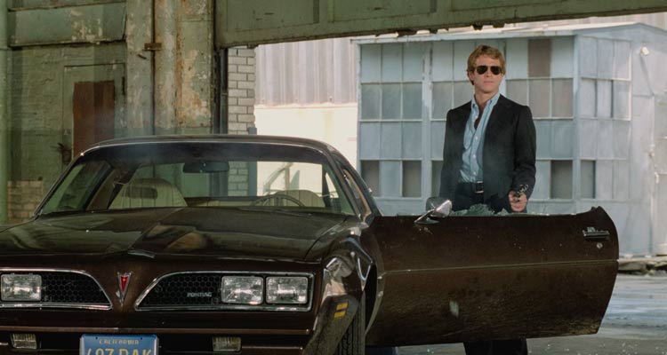 The Driver 1978 Movie Scene Ryan O'Neal as The Driver shooting over his car, a black 1977 Pontiac Firebird Esprit