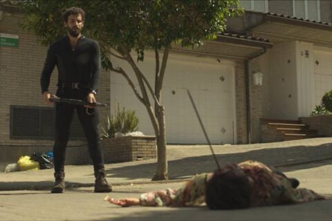 Apocalypse Z The Beginning of the End 2024 Movie Scene Francisco Ortiz as Manel standing over the body of a zombie he just killed on the street