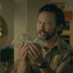 Greedy People 2024 Movie Scene Joseph Gordon-Levitt as Terry holding wads of cash in his hands to his partner