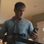 Coldwater 2025 Series Scene Andrew Lincoln as John looking at the phone while holding a rifle