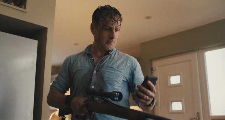 Coldwater 2025 Series Scene Andrew Lincoln as John looking at the phone while holding a rifle