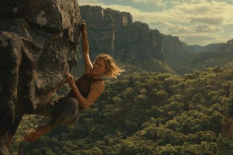 Apex 2026 Movie Scene Charlize Theron as Sasha hanging on the edge of the cliff