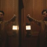 Hokum 2026 Movie Scene Adam Scott as Ohm Bauman holding a lantern in the elevator of the haunted hotel Bilberry Woods
