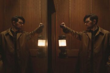 Hokum 2026 Movie Scene Adam Scott as Ohm Bauman holding a lantern in the elevator of the haunted hotel Bilberry Woods