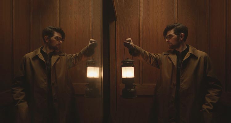 Hokum 2026 Movie Scene Adam Scott as Ohm Bauman holding a lantern in the elevator of the haunted hotel Bilberry Woods
