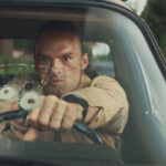 The Orphans 2025 Movie Scene Alban Lenoir as Gabriel Stenne Gab shooting through his windshield at the bad guys
