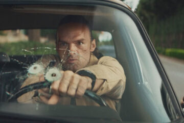 The Orphans 2025 Movie Scene Alban Lenoir as Gabriel Stenne Gab shooting through his windshield at the bad guys