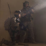 Warfare 2025 Movie Scene D'Pharaoh Woon-A-Tai as Ray and Will Poulter as Erik standing next to the front door calling for backup armed with M4A1 Carbines